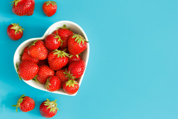 Fresh strawberries in a heart-shaped bowl on blue background.