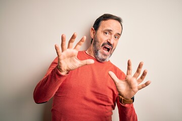 Poster - Middle age hoary man wearing casual orange sweater standing over isolated white background afraid and terrified with fear expression stop gesture with hands, shouting in shock. Panic concept.