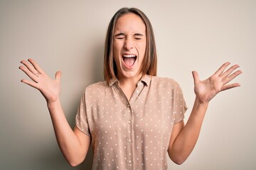 Young beautiful woman wearing casual shirt standing over isolated white background celebrating mad and crazy for success with arms raised and closed eyes screaming excited. Winner concept