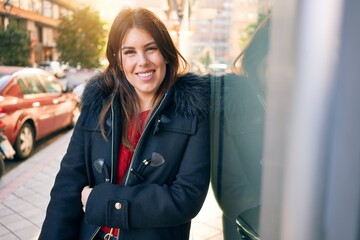 Wall Mural - Young beautiful brunette woman smiling happy and confident. Standing with smile on face leaning on the wall at street of city