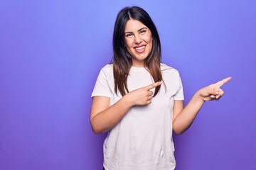 Sticker - Young beautiful brunette woman wearing casual t-shirt standing over purple background smiling and looking at the camera pointing with two hands and fingers to the side.