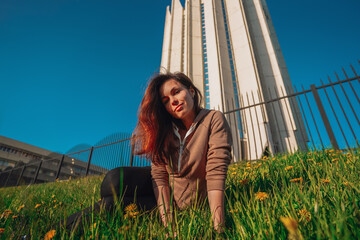 A young girl with long hair sits in a field of dandelions on a Sunny happy day against the backdrop of a futuristic sk