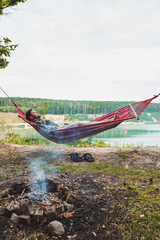 Wall Mural - man laying on hammock at lake beach near camp fire