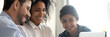 Three multi ethnic colleagues involved in learning new corporate business application seated together in coworking desk, teamwork mentoring concept. Horizontal photo banner for website header design