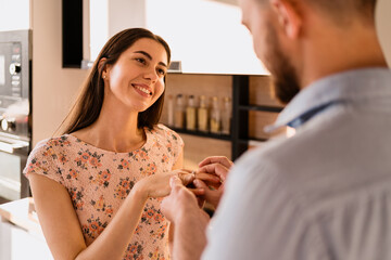 Wall Mural - Woman smiling, happy while her man Putting On Engagement Ring To Her Finger On A Romantic Date at home