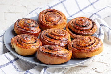 Wall Mural - baked cinnamon buns on grey plate on light background with checkered napkin