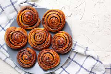 Wall Mural - baked cinnamon buns on grey plate on light background with checkered napkin