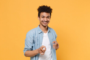 Wall Mural - Smiling young african american guy in casual blue shirt posing isolated on yellow wall background studio portrait. People emotions lifestyle concept. Mock up copy space. Point index fingers on camera.