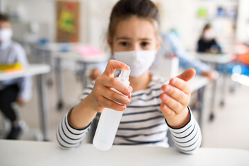 Poster - Small girl with face mask at school after covid-19 lockdown, disinfecting hands.