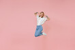 Cheerful young blonde woman girl in casual striped shirt posing isolated on pastel pink background studio portrait. People emotions lifestyle concept. Mock up copy space. Jumping, put hands on head.