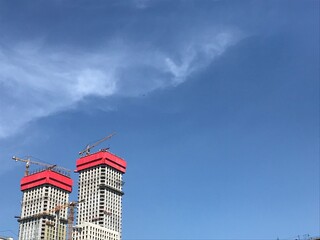 the construction of two towers of a skyscraper with yellow high-rise cranes against the blue sky