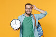 © ViDi Studio - Puzzled young man student in casual clothes glasses with backpack isolated on yellow background. Education in high school university college concept. Mock up copy space. Hold clock, put hand on head.