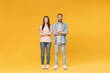 © ViDi Studio - Smiling young couple two friends guy girl in pastel blue casual clothes posing isolated on yellow wall background studio portrait. People lifestyle concept. Mock up copy space. Holding hands crossed.