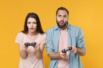 Poster - Shocked young couple two friends guy girl in pastel blue casual clothes posing isolated on yellow background studio portrait. People lifestyle concept. Mock up copy space. Play game with joystick.