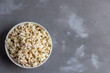 © dashtik - Popcorn in white bowl on grey table. Top view with copyspace