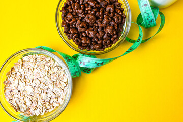 Two bowls with quick breakfast of chocolate cornflakes and oat meal with centimeter tape on bright yellow baclground. Copy space