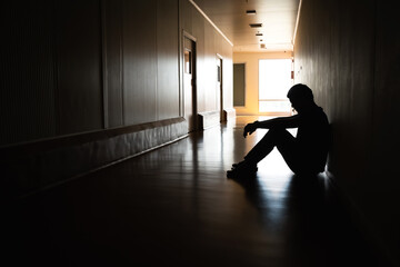 Silhouette of depressed man sitting on walkway of residence building. Sad man, Cry, drama, lonely and unhappy concept.