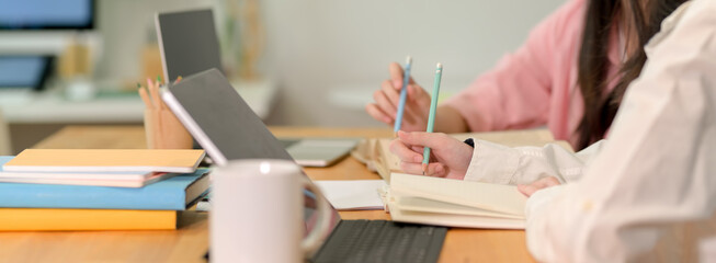 Female college students preparing their upcoming exam together with digital tablet, book and stationery