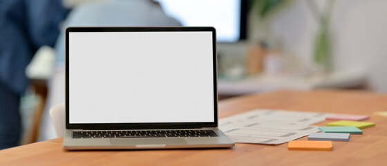 UI developer workspace with blank screen laptop, paperwork and notepad on wooden desk
