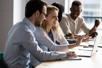 In coworking modern room caucasian woman and man working on common project prepare presentation using laptop discuss new business program, having fun enjoy friendly talk, mentoring cooperation concept