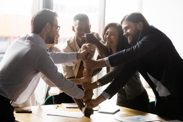 Poster - Korean African Caucasian mature and young diverse five overjoyed mates having fun participate in teambuilding activity laughing stacked fists together show team spirit, synergy, common success concept