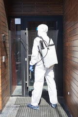 Back view full length portrait of male worker wearing protective suit spraying chemicals over building outdoors during disinfection