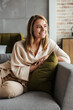 © Drobot Dean - Image of woman smiling and looking aside while sitting on sofa