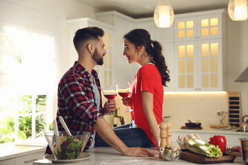 Poster - Lovely young couple drinking wine while cooking together at kitchen