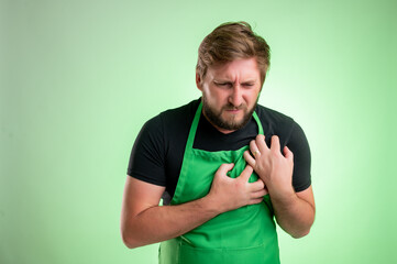 Supermarket employee with green apron and black t-shirt suffering heart ache or breast pain, cardiac problems