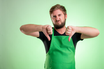 Supermarket employee with green apron and black t-shirt showing double dislike