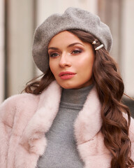 beautiful caucasian woman with long brunette hair in pink fur coat and gray beret walking in city. o