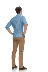 back view of concerned casual guy holding hands on hips