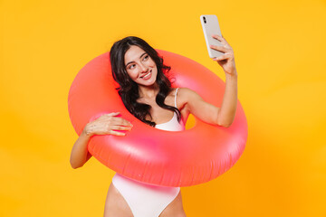 Wall Mural - Image of woman with rubber ring smiling and taking selfie on cellphone