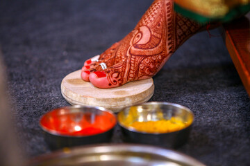 Indian wedding bride right foot on rock with two bowl of haldi kumkum