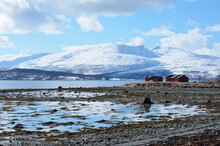 Majestic Snowy Mountain And Blue Sky Landscape Near Calm Fjord With Red Boathouses