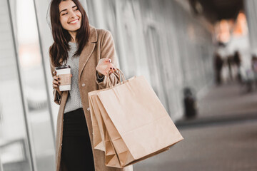 Beautiful fashionable woman with shopping bags and coffee walking near mall.