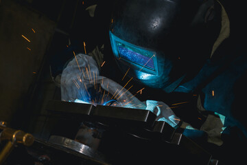 Close-up blacksmith welder in protective mask works with metal steel and iron using a welding machine, bright sparks and flashes. Welder uses a mask to protect your eyes from sparks.