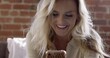 © vesperstock - CU Young blonde woman smiles while using a smart phone in an urban apartment space. Brick wall background