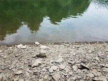 Broken Grey Rocks And Water At Shore Of River Or Lake