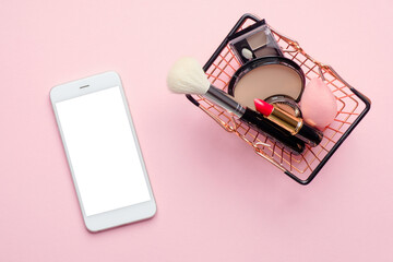 Shopping online app concept. Flat lay mobile phone with blank screen mockup and shopping basket full of makeup cosmetics on pink background. Flat lay, top view.