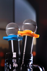 Two microphones stand in an empty beer mug. The concept of a karaoke restaurant. Vertical photo on a dark background. Copy of the space.