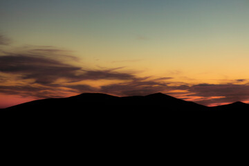 Wall Mural - mountain ridge silhouette landscape background of moody dramatic weather time with soft color orange sunset lighting