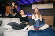 © gorynvd - Good-looking cheerful young female friends sitting on the couch in the contemporary apartment and enjoying video games