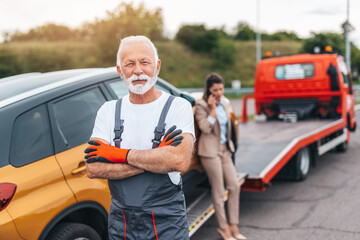 Wall Mural - Confident senior man worker in towing service standing in front of his truck with crossed arms and looking at camera.