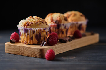 Three berry chocolate muffins on a wooden board, decorated with berries and chocolate.