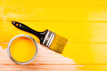 Opened Can Of Paint With Brush On Yellow Freshly Painted Wooden Background. Renovation Concept. Vertical Photo.