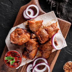 Wall Mural - Grilled meat or shish kebab, shashlik with tomato sauce on wooden board over dark stone background. Top view