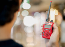 The Male Hand Holding With A Red Walkie Talkie Or Portable Radio Transceiver For Communication.