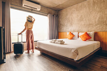 Portrait Of Tourist Woman Standing Nearly Window, Looking To Beautiful View With Her Luggage In Hotel Bedroom After Check-in. Conceptual Of Woman Lifestyle When Traveling On Her Vacation.