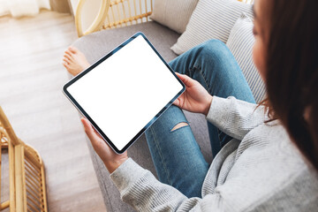 Top view mockup image of a woman holding black tablet pc with blank desktop white screen while lying on a sofa at home